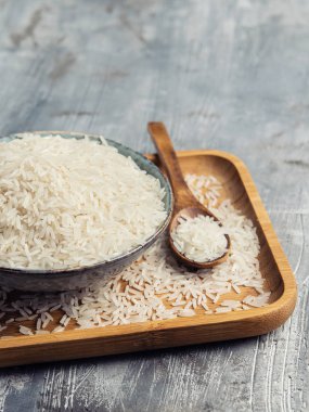 Gri arka plan üzerinde tahta kaşıkla seramik kase çiğ beyaz pirinç. Wabi Sabi tarzı. Uzay kopyalayın. Dikey.