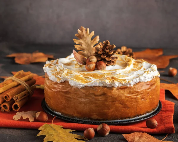 Homemade Pumpkin Cheesecake with Marshmallow Meringue Topping decorated with pinecones and autumn leaves over dark background. Autumn Decoration.