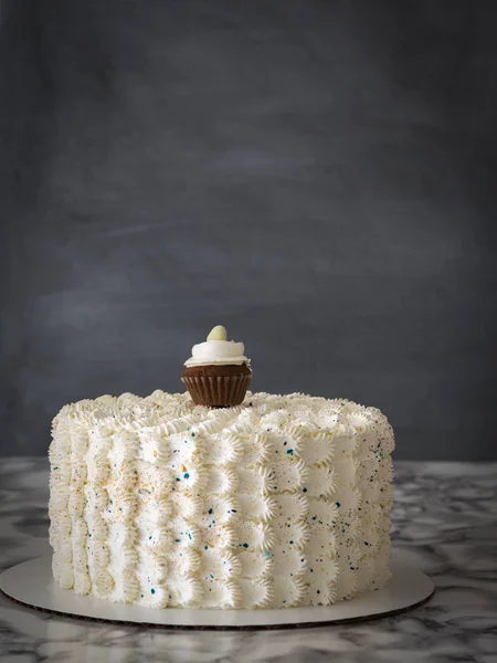 White buttercream birthday cake with a mini cupcake on marble table. Vertical. Copy space.