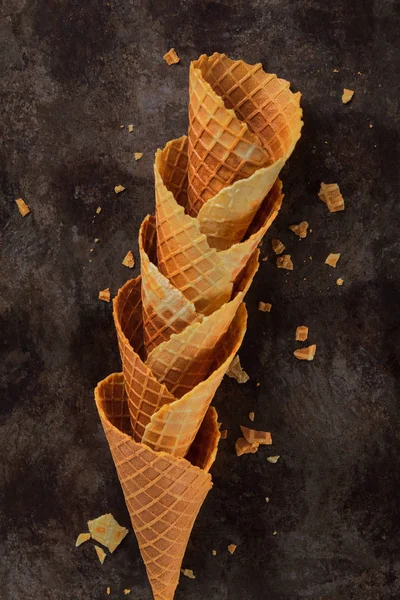 Homemade stacked empty cornets or ice cream waffle cones on dark background. Selective focus. Minimal flat lay composition with copy space.