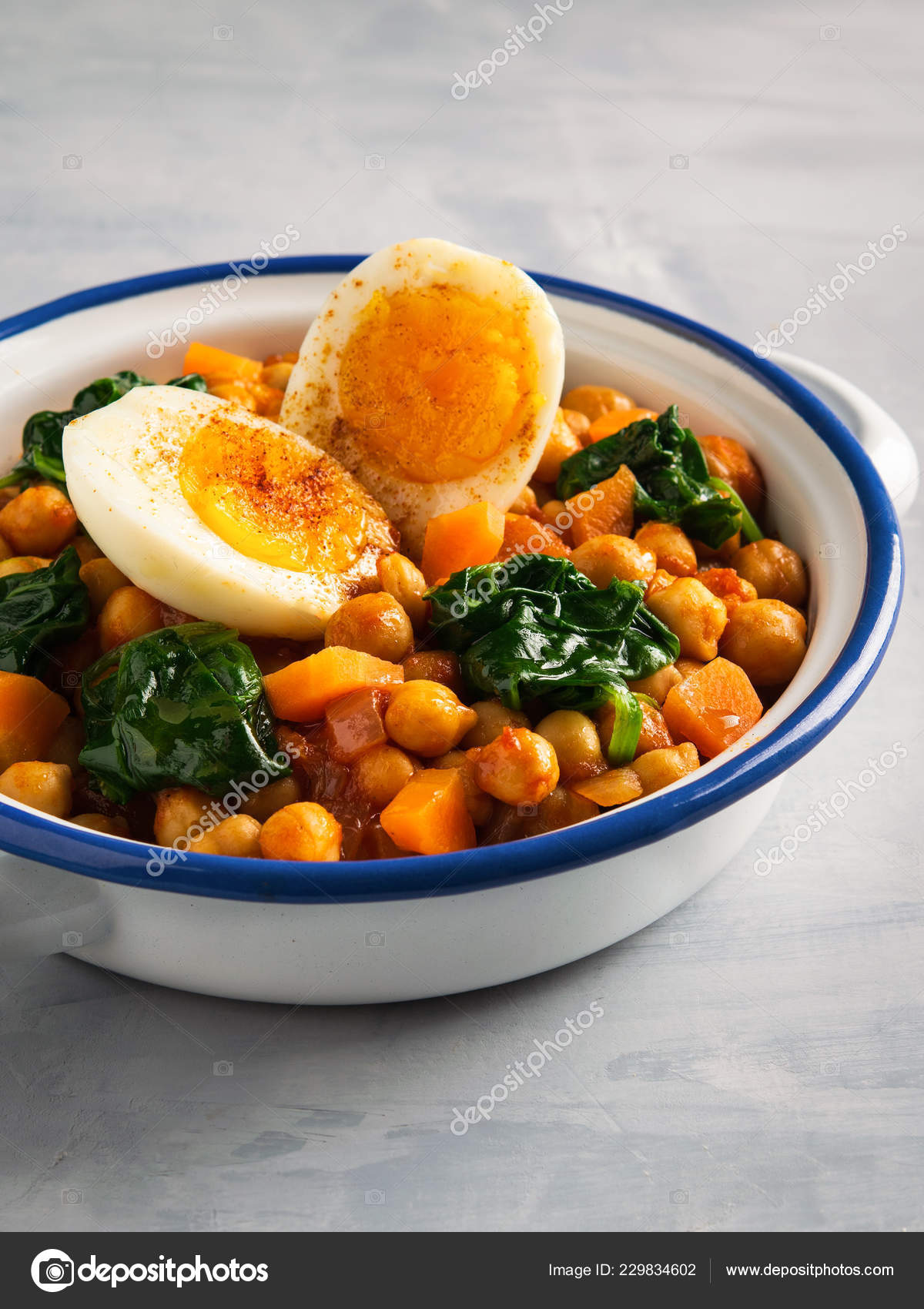 Spanish chickpea and spinach stew with eggs on light gray background