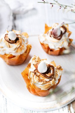 Phyllo dough cups with meringue and melted chocolate close up on a plate. White rustic background with space for your text. with meringue and melted chocolate close up on a plate. White rustic background with space for your text.
