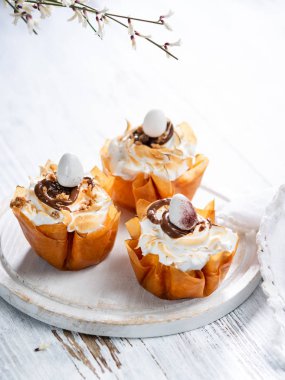 Phyllo dough cups with meringue and melted chocolate close up on a plate. White rustic background with space for your text. with meringue and melted chocolate close up on a plate. White rustic background with space for your text.