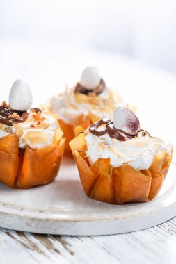 Beze ve eritilmiş çikolata ile Fancy Phyllo hamur bardak yakın bir tabak ta. Metniniz için alan içeren beyaz rustik arka plan.