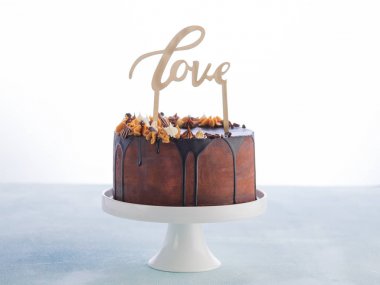 Eritme çikolata ganache ile düğün pastası ve metin alanı ile beyaz bir arka plan üzerinde ahşap caketopper aşk. Sevgililer günü kutlama kavramı. Trendy damla kek.