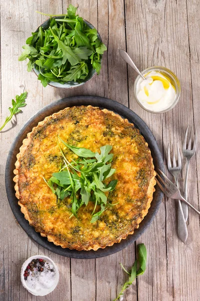 Quiche with arugula, onion, spinach, mozzarella, feta and sauce on rustic background, top view. Homemade, traditional french quiche pie. — Stock Photo, Image