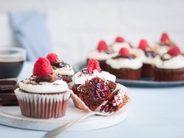 Çikolatalı kekler, masada bir fincan kahve ve taze ahududu ile ikiye kesilmiş cupcake, uzay metin ile hafif arka plan.