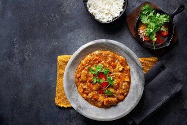 Tavuklu tikka masala baharatlı körili et yemeği marber tabağında pilav ve koyu gri arka planda baharatlar. Hint yemeği tarifi.