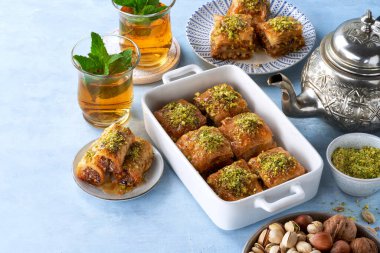 Baklava, ortadoğu tatları, kurutulmuş hurma, şam fıstığı, bal, açık mavi arka planda nane çayı. Seçici odaklanma. Ramazan.