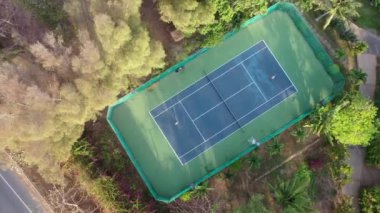 Kızlar gün batımında kortta tenis oynuyorlar. Havadan güzel bahçedeki büyük tenis kortuna. Etrafta bir sürü yeşil ağaç var. Tropik yemyeşil doğa. Spor dışarıda devam ediyor. Tatil faaliyetleri 