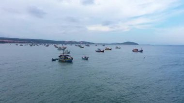 Bulutlu bir günde deniz manzarası. Yüzlerce renkli balıkçı gemisiyle mavi okyanus. Drone deniz üzerindeki kuşu takip ediyor. Gökyüzü ve suyun gri ve mavi renkleri