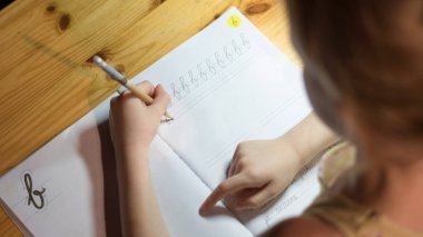 Altı yaşında bir kız bir defter bir masa lambası altında yazma alıştırma