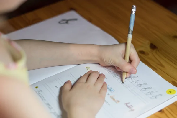 一个六岁的女孩正在用台灯在笔记本上练习写字 — 图库照片