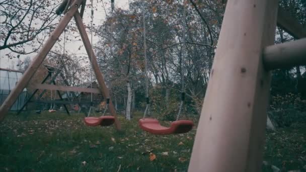 子供赤スイング孤独な子供のいない古いファームで秋の曇り日に風に揺れて — ストック動画