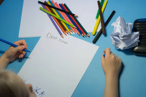 Little girl with pencils and felt-tip pens is writing a letter to Santa
