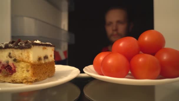 カクテル トマトやおいしいケーキ ボケ男ビュー内の冷蔵庫から健康食品の難しい選択 トマトに勝つ — ストック動画