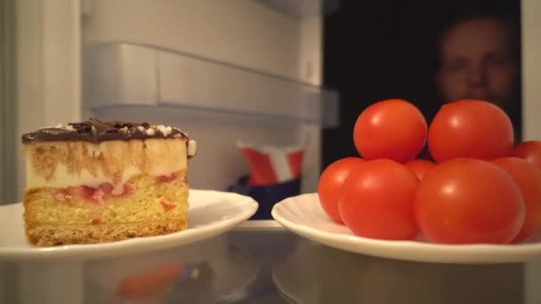 鸡尾酒番茄或美味蛋糕 一个艰难的选择健康食品从冰箱 里面看 男人失去了关注 蛋糕赢取 — 图库视频影像