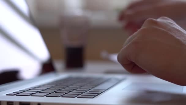 Gros plan des mains travaillant et tapant sur un clavier d'ordinateur portable avec des touches noires, dans le processus de travail, un homme regarde les documents papier 