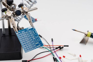 LED (ışık yayan diyot), teller ve havya arka planda teknolojik lehimleme işlemi önce yardım lehimleme içinde mavi devre levhasını eller (üçüncü el veya yardımcı klip aracı).