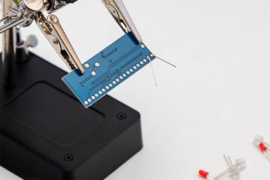 Yardım lehimleme içinde mavi devre levhasını (üçüncü el veya yardımcı klip aracı) beyaz ve kırmızı LED (ışık yayan diyot) teknolojik lehimleme işlemi önce ışık arka plan üzerinde eller.