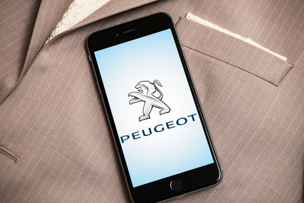 Ekranda Fransız araba fabrikası Peugeot logosu ile siyah iPhone. Araba fabrikası simgesi. Arka planda iş kıyafeti