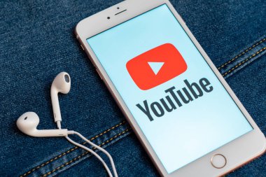 Tallinn/Estonya - 19 Mayıs 2019: Ekranda sosyal medya Youtube kırmızı logosu ile beyaz iphone. Sosyal medya simgesi. Denim kot arka plan. Pazarlama konsepti veya haber medyası illüstrasyonu.