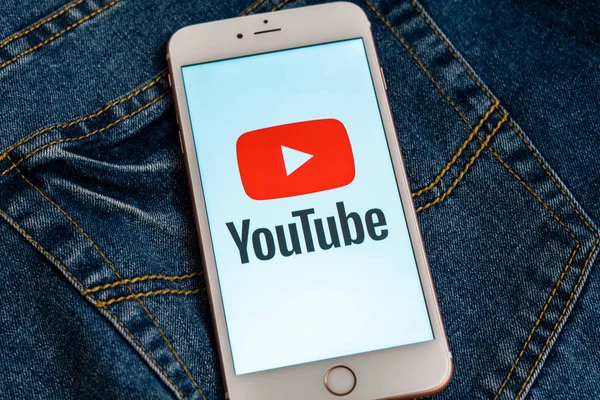 Tallinn/Estonya - 19 Mayıs 2019: Ekranda sosyal medya Youtube kırmızı logosu ile beyaz iphone. Sosyal medya simgesi. Denim kot arka plan. Pazarlama konsepti veya haber medyası illüstrasyonu.