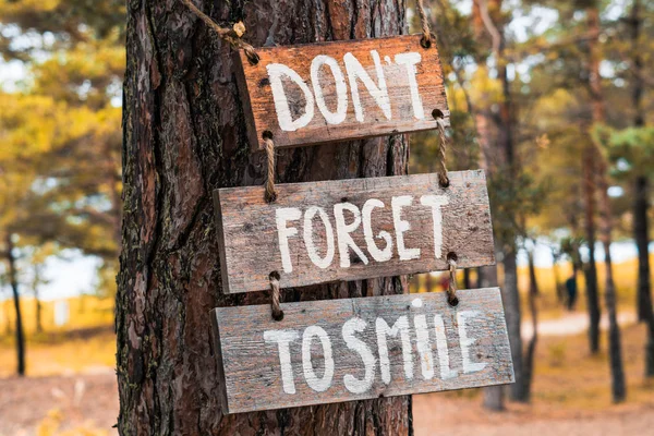 Sebuah tanda motivasi kayu "Jangan lupa untuk tersenyum". di pohon pinus Stok Foto Bebas Royalti