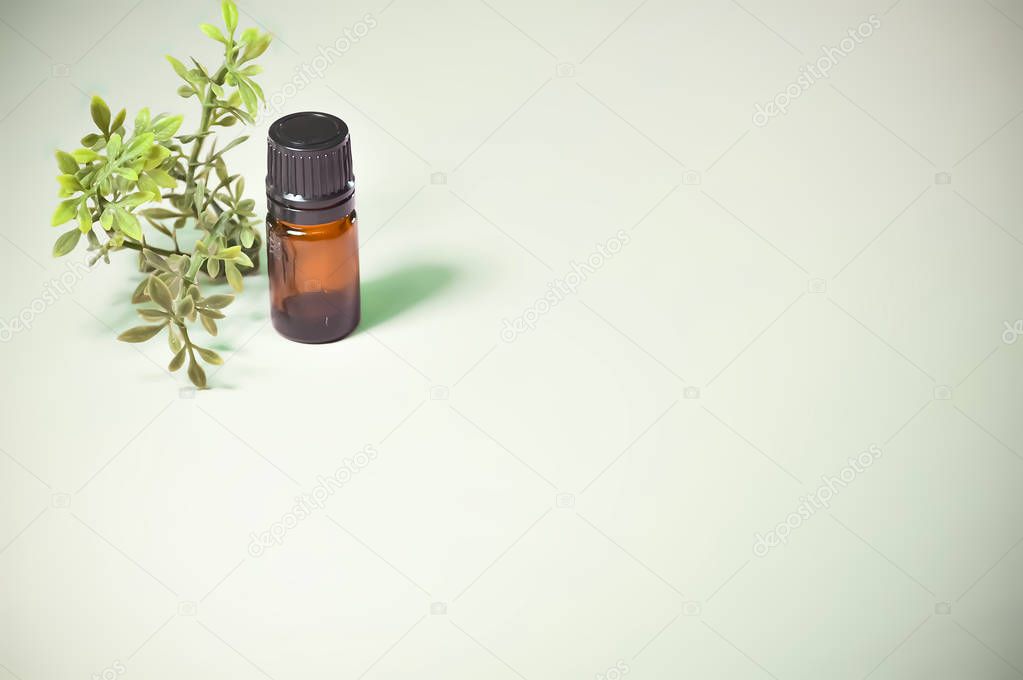 Small Brown Glass Essential Oil Bottle with Plant on Light Green Background