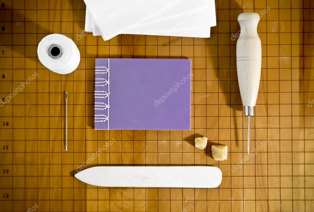 Bookbinding Materials with Small Purple Notebook on Wood Surface