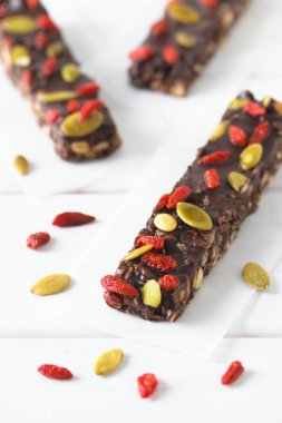 Granola, fındık, balkabağı, goji üzümü ve chia tohumlu vejetaryen çikolata. Ev yapımı atıştırmalık. Beyaz ahşap arka planda süper enerji çubukları.