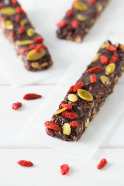 Granola, fındık, balkabağı, goji üzümü ve chia tohumlu vejetaryen çikolata. Ev yapımı atıştırmalık. Beyaz ahşap arka planda süper enerji çubukları.