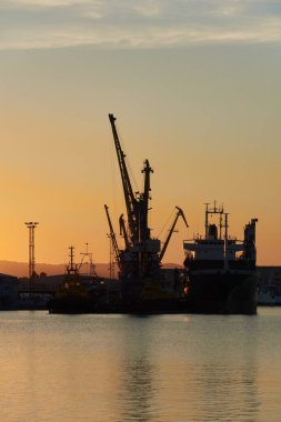 Vinçler ve gemiler gün batımında limanda