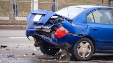 Yan görüş. Mavi arabanın arkası hasar görmüş ve yolda kaza sonucu kırılmış.. 