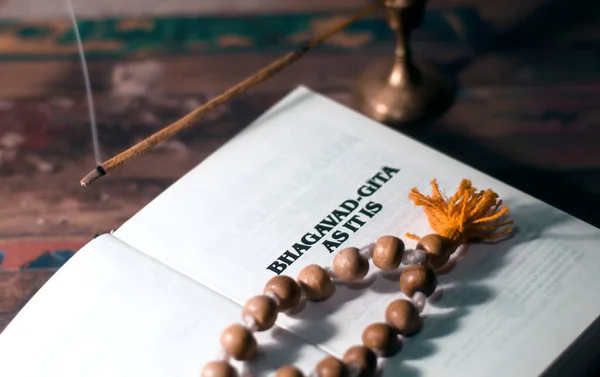 Bhagavad Gita ve tespihi ahşap bir masanın üzerinde tütsü ve tütsü içiliyor..