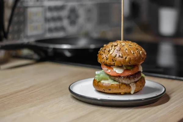 Tasty burger with grilled beef, lettuce and mayonnaise served on ceramic plate on regular bright kitchen, close up, with copyspace — Stock Photo, Image