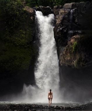 Ormanlardaki şelaleye bakan genç bir kadın.