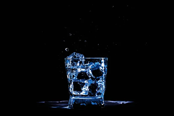 Cubo de hielo cae en un vaso de agua azul o una bebida en un negro —  Fotos de Stock