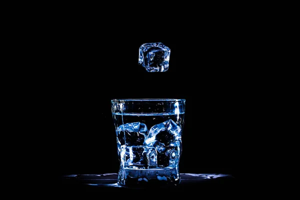 Cubo de hielo cae en un vaso de agua azul o una bebida en un negro —  Fotos de Stock