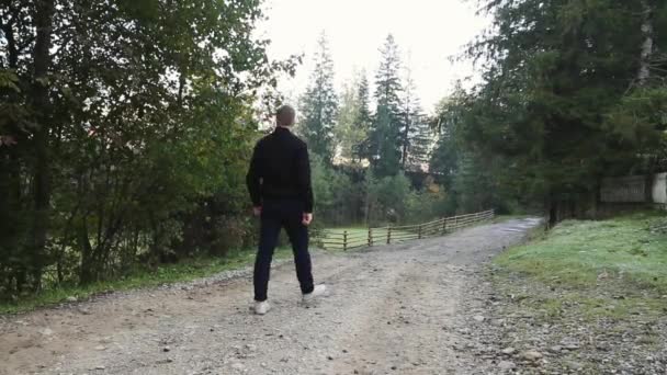 年轻的家伙走在乡间的泥土路在山区和木材 — 图库视频影像