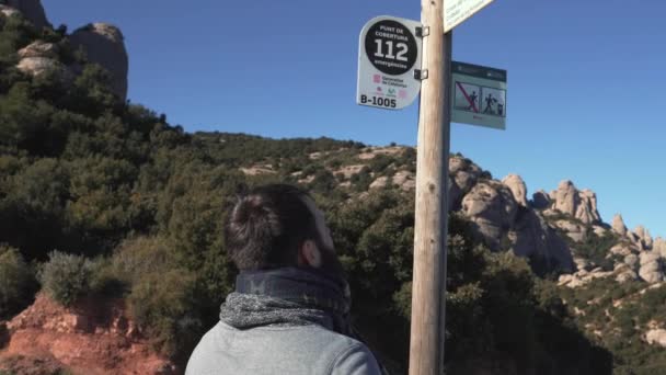 De man kijkt naar de borden op de berg om te beslissen waar hij moet gaan — Stockvideo