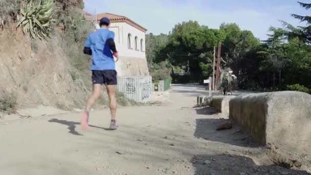 Joven deportista corre por la empinada pendiente de un camino de tierra — Vídeos de Stock