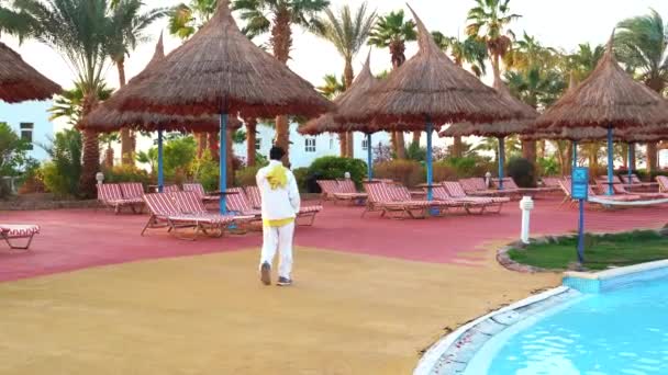 Hotel employee walks along the pool with sunbeds — Stock Video