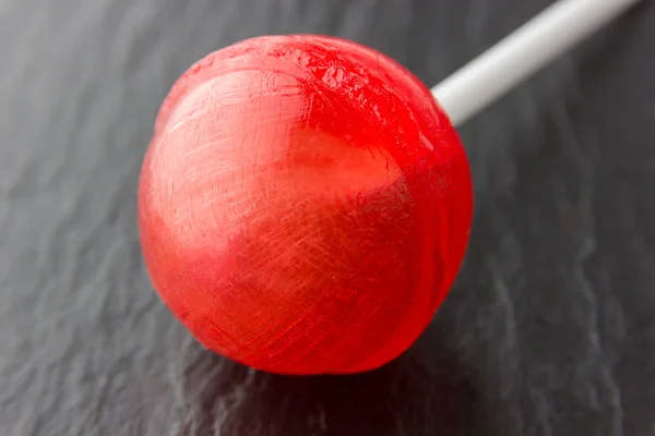 Round lollipop on a stick of red color. Candy on a stick lies on a surface of shale stone.