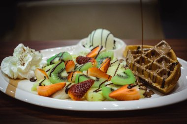 Klasik Belçika waffle, çilek, muz, kivi ve ananas dilimleri ile servis. Zengin çikolata ile drizzled, yanında dondurma ile servis.