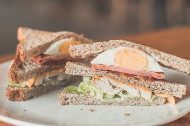 Club Sandwich Fırında kavrulmuş tavuk, dilimlenmiş füme hindi, yumurta ve peynir ile çift katlı kepekli sandviç. 