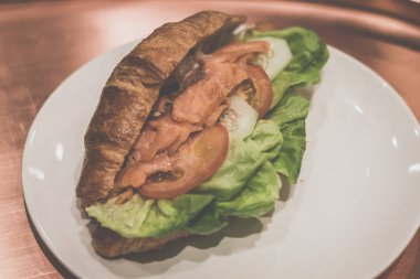 Beyaz porselen plaka üzerinde füme slamon ve marul ve domates ile Kruvasan