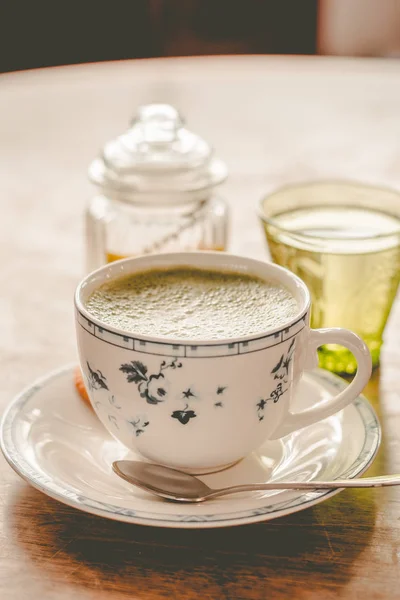 green tea matcha soy latte in a china cup with brown sugar and a glass of water on the side