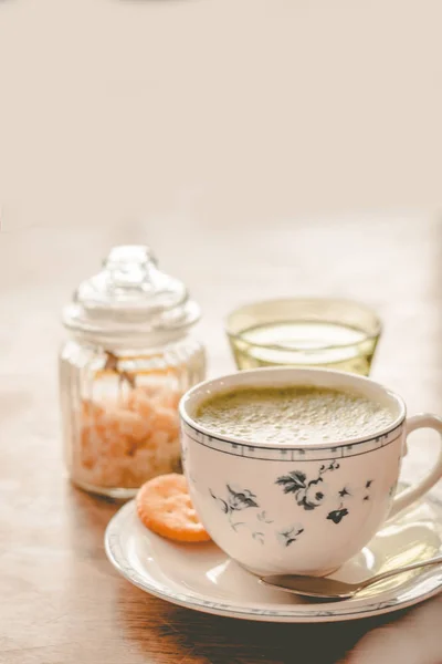 green tea matcha soy latte in a china cup with brown sugar and a glass of water on the side