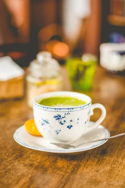 green tea matcha soy latte in a china cup with brown sugar and a glass of water on the side